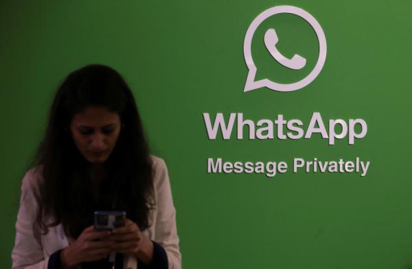 A woman uses her phone next to a logo of the WhatsApp application during Global Fintech Fest in Mumbai